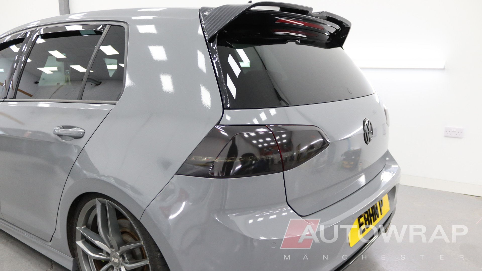 A nardo grey VW Golf with a dark tint on the rear windows and lights. It is sat in a workshop, tilted towards the camera.
