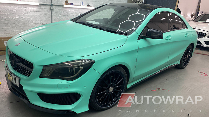 A Mercedes CLA wrapped ina bright mint green colour. The car is posed on an angle in an industrial unit.