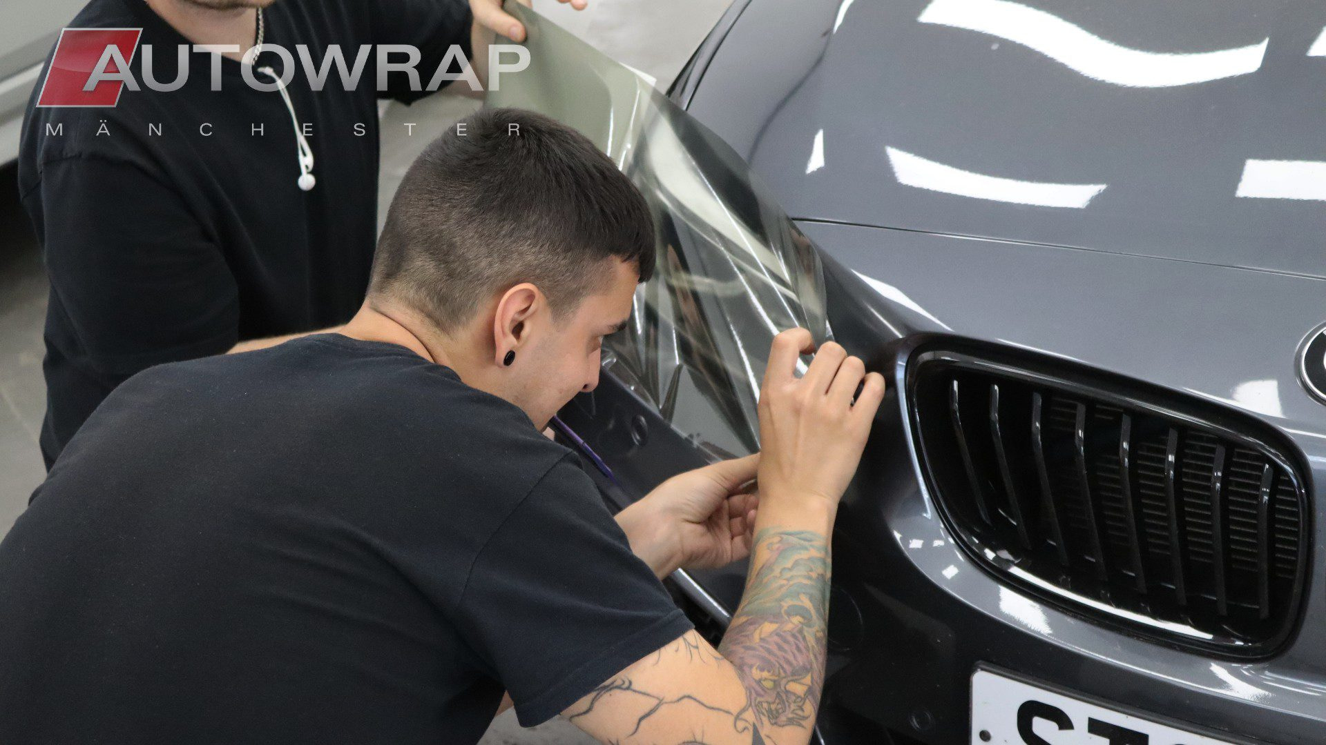 a wrapper applying film to the front headlights of a grey car.